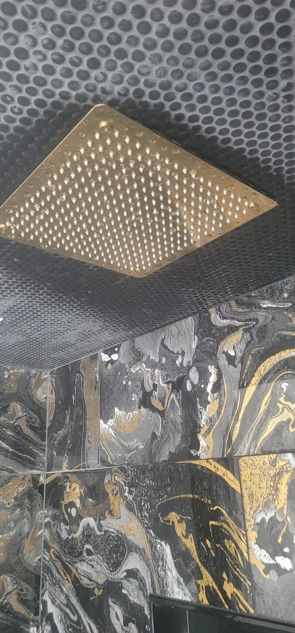 Large brass rain shower head set into a tiled ceiling