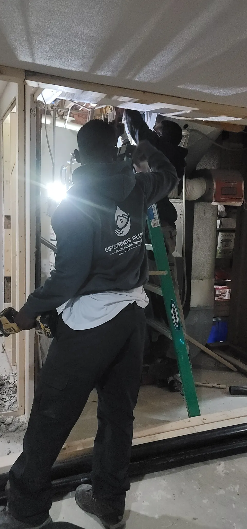 GiftedHands plumber in a branded hoodie working overhead