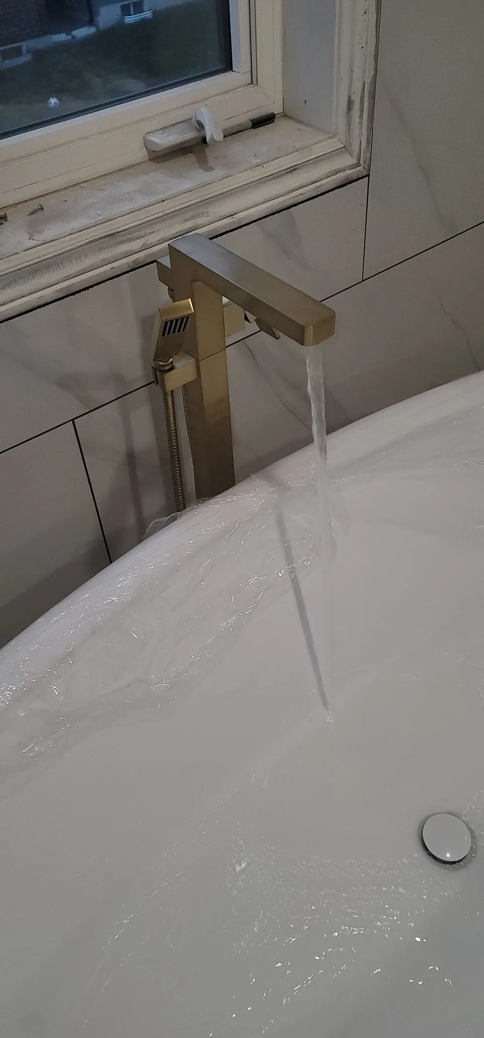 Gold floor-mounted tub filler running into a freestanding tub