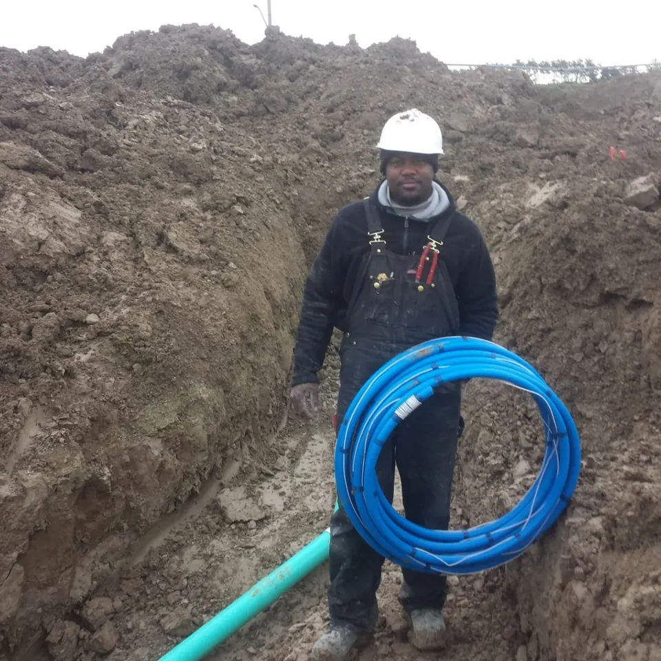 Plumber in a trench with a coil of blue water service pipe