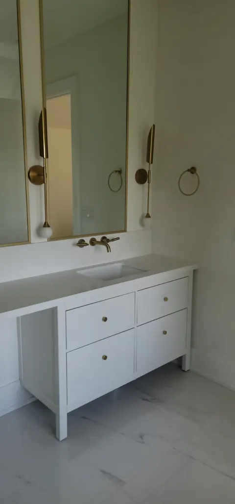 White vanity with a brass wall-mounted faucet and round mirror lights